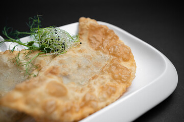 cheburek or fried dough pie with meat feeling and sauce on black background