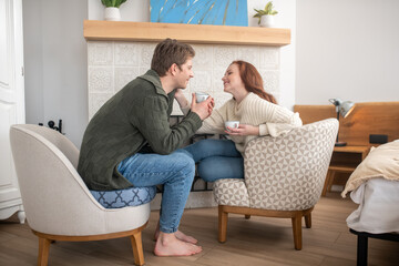 Smiling man and touching woman drinking coffee near fireplace