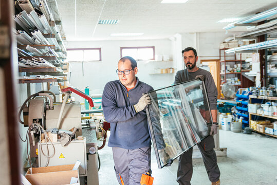 Male workers with aluminum window glass in workshop