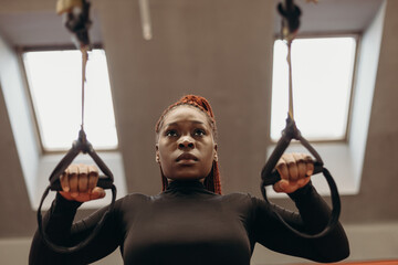 Black sportswoman doing exercises on TRX straps in gym
