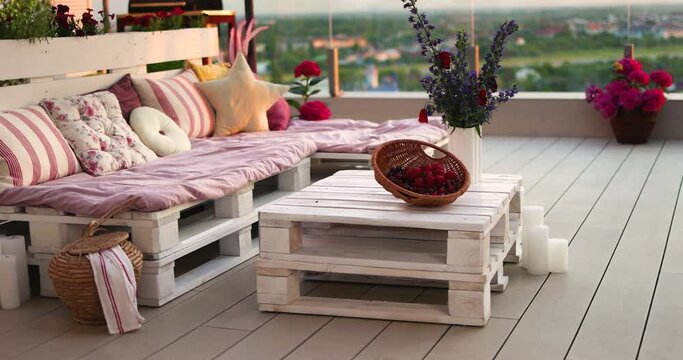 a lounge zone hand crafted from wooden pallets on rooftop patio, decorated with pillows, eco recycling