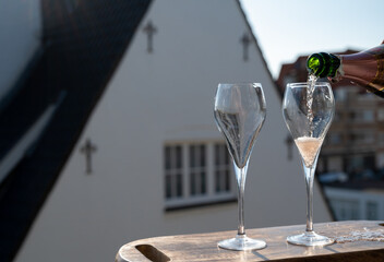 Pouring of rose champagne sparkling wine in flute glasses on outdoor terrace in France