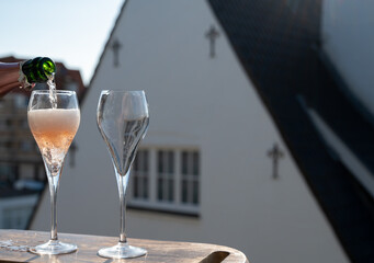 Pouring of rose champagne sparkling wine in flute glasses on outdoor terrace in France
