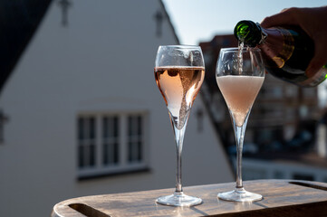Pouring of rose champagne sparkling wine in flute glasses on outdoor terrace in France