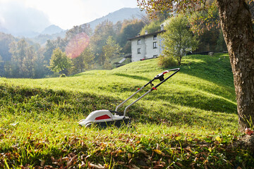 Lawn mower, brushcutter on green grass in garden in front of italian mountains, sunny autumn day....