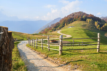 Picturesque Alps autumn landscape, wooden fence and mountain hills in Lombardy, Italy. Tourist adventure, colorful autumn scene