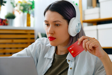 Young woman in headphones using internet bank service on laptop