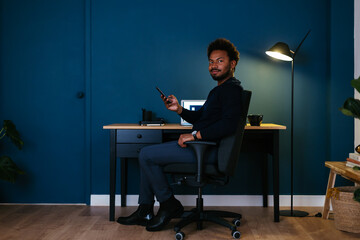 Black freelancer with smartphone sitting near desk