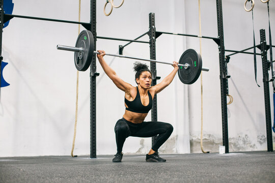 Hispanic female weightlifter squatting with barbell