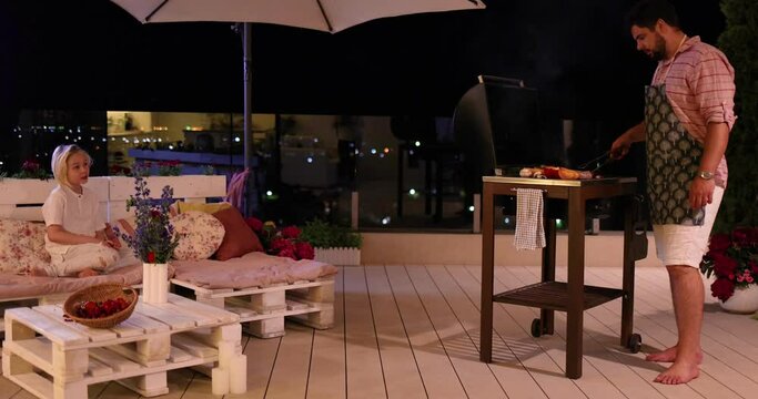 cheerful father and son relaxing on rooftop patio, grilling food on cozy courtyard at home