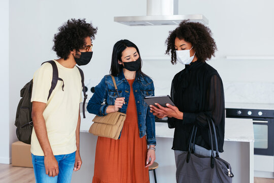 Diverse couple and realtor examining rent options on tablet during epidemic