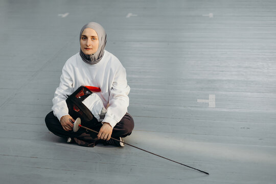 Calm Muslim sportswoman with fencing sword and mask in gym