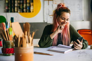Cheerful craftswoman using smartphone in pottery 