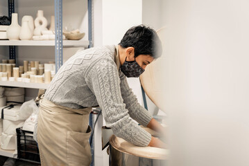Woman potter with mask putting pottery in kiln.