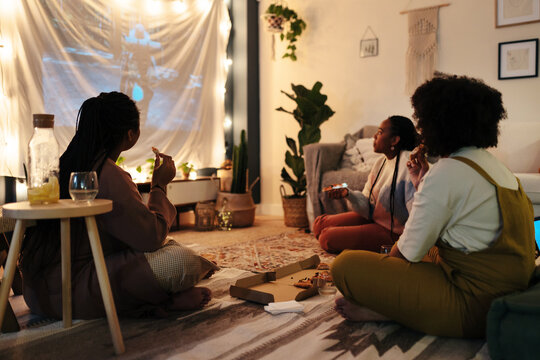 Black girlfriends with pizza watching film at night