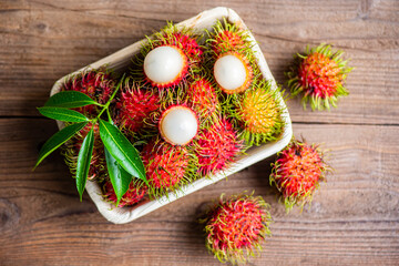 Rambutan fruit on plate and wooden background harvest from the garden, Fresh and ripe rambutan sweet tropical fruit peeled rambutan with leaves
