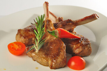Rack of lamb, with tomatoes red pepper and rosemary on white plate closeup