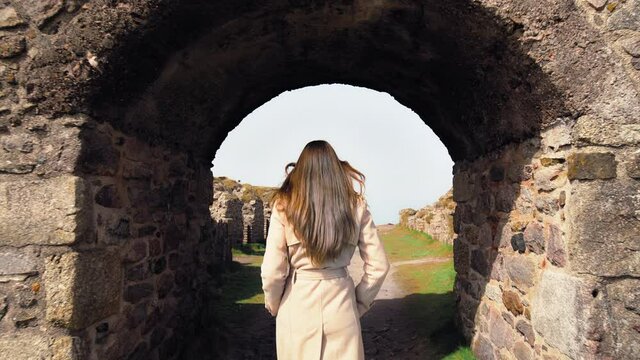 A fashionable girl in a coat walking through ruins of a castle in Cornwall in 4K. Crowns Engine Houses, Botallack Mine, ruins of an old ancient English building in 4k.