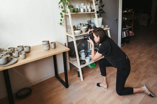 Female artisan photographs ceramic products.