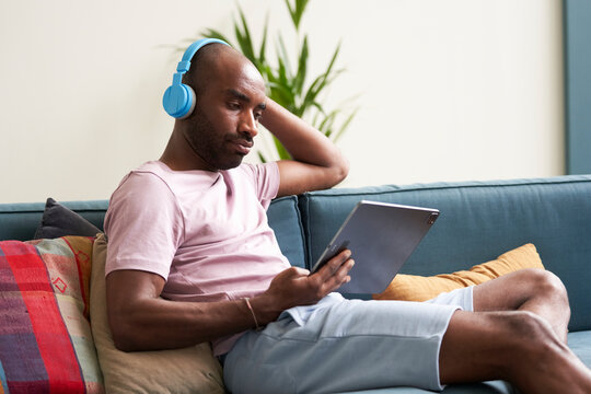 Relaxed guy with tablet and headphones watching movie on sofa