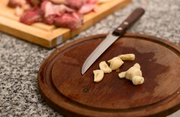 Sliced garlic on a wooden plate with red meat in the background. Close up.