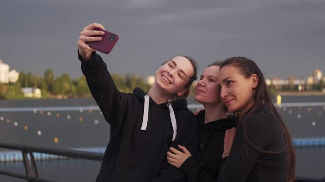 Three young girls hold a phone and take a selfie against the background of the sea in the afternoon