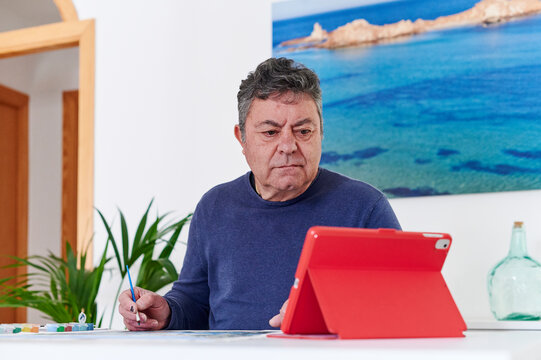 Mature man painting to a tutorial on a tablet