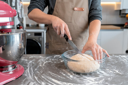 Man cutting the raw dough of a loaf of bread in a kitchen