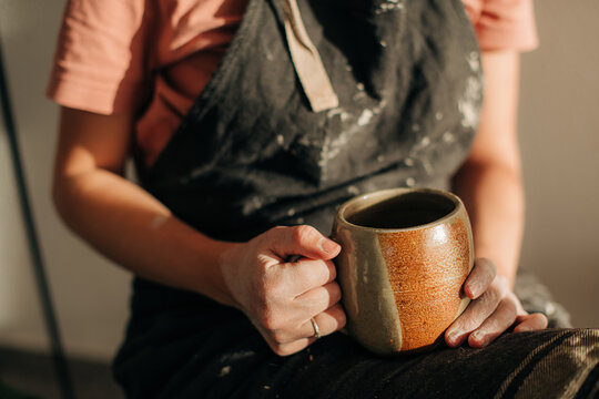 Female potter in apron caked with clay holding a cup of tea