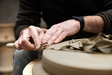 Artisan sitting on a workshop while removing excess material from the surface of a ceramic piece
