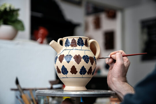 Person painting a ceramic vase with leaf shapes in a workshop.