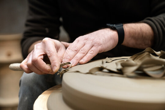 Artisan sitting on a workshop while removing excess material from the surface of a ceramic piece