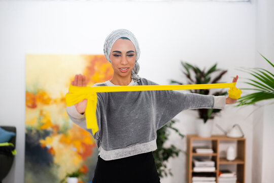 Muslim woman exercising with resistance band at home