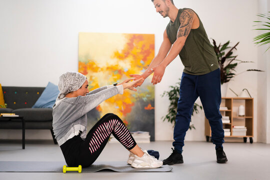 Cheerful Arab woman doing abdominal crunches near husband