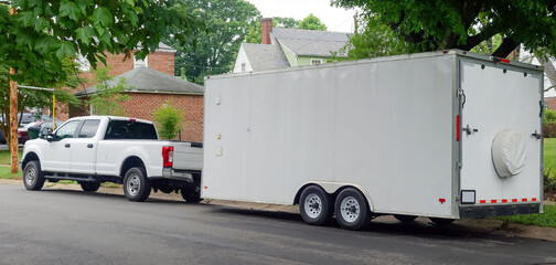 White pickup truck and large utility trailer parked on residential city street.