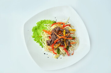 Plate of noodles with meat and vegetables isolated on white background, top view