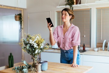 Young florist taking photo of flowers in kitchen
