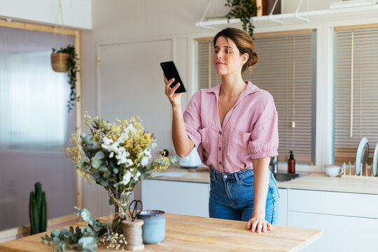 Young florist taking photo of flowers in kitchen