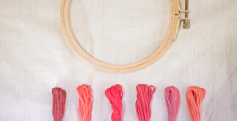 The linen Canvas for embroidery with a cross embroidered in a round wooden hoop, multi-tone pink-colored thread