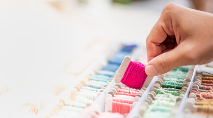 Close up hands of tailor woman holding vivid pink threads and different colors in the box put on table and prepare to use with white cotton and frame wood.