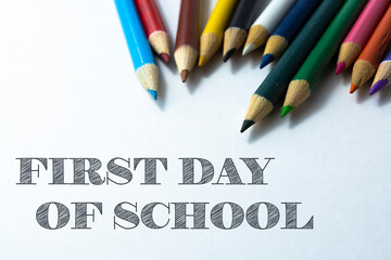Text FIRST DAY OF SCHOOL on white background with colorful pencils. Educational concept.