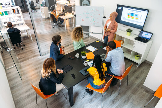 Unrecognizable diverse partners discussing project against statistics on monitor