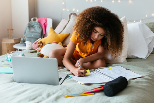 Schoolkid with laptop doing learning online on bed