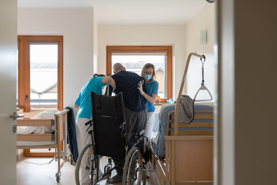 Nurses Helping Patient To Get In Wheelchair