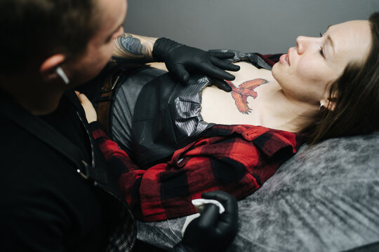 Woman with red bird tattoo preparing for session in tattoo studio