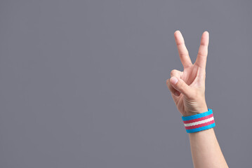 Young hand making the victory sign, wearing a transgender flag bracelet