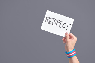 Hand with a transgender flag bracelet holding a paper with a message: respect