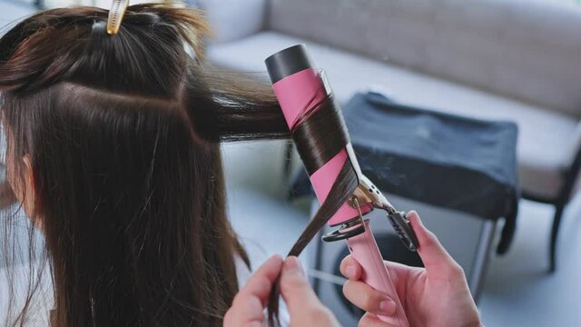 Close up of Hairdresser make curly to customer's hair in beauty salon.