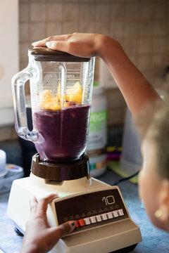 Young girl pressing the start button on a blender.
