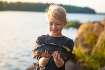 Boy smiles holding fish he caught on fishing trip vacation
